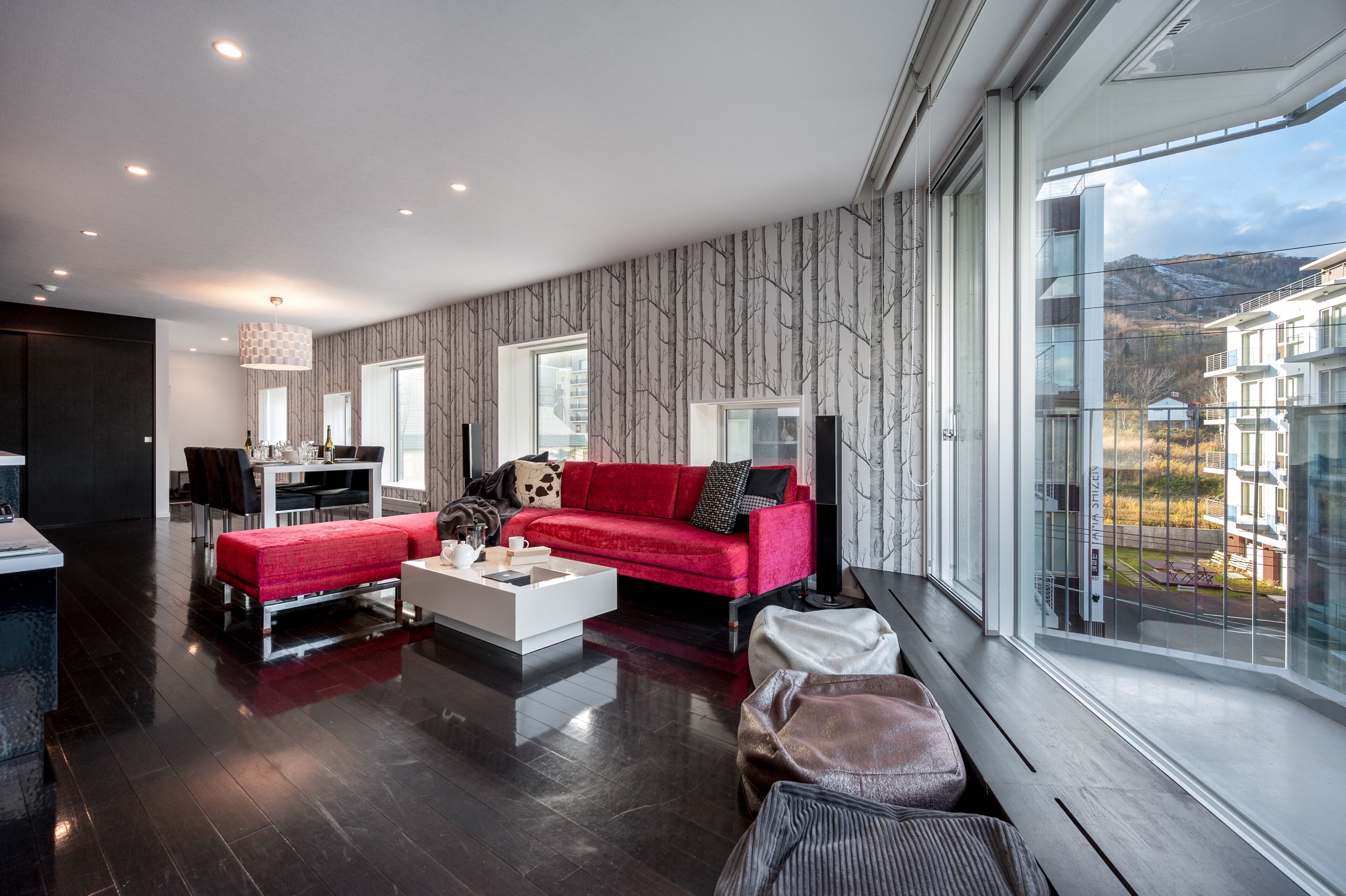 A modern living room with a red sofa, white coffee table, and a dining area with a chandelier.