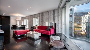 A modern living room with a red sofa, white coffee table, and a dining area with a chandelier.