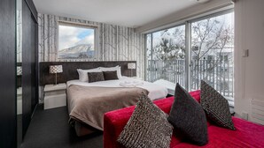 A modern hotel room with a large bed, a red sofa, and a view of a snowy mountain. - Kira Kira Suites by H2 Life (Kutchan)
