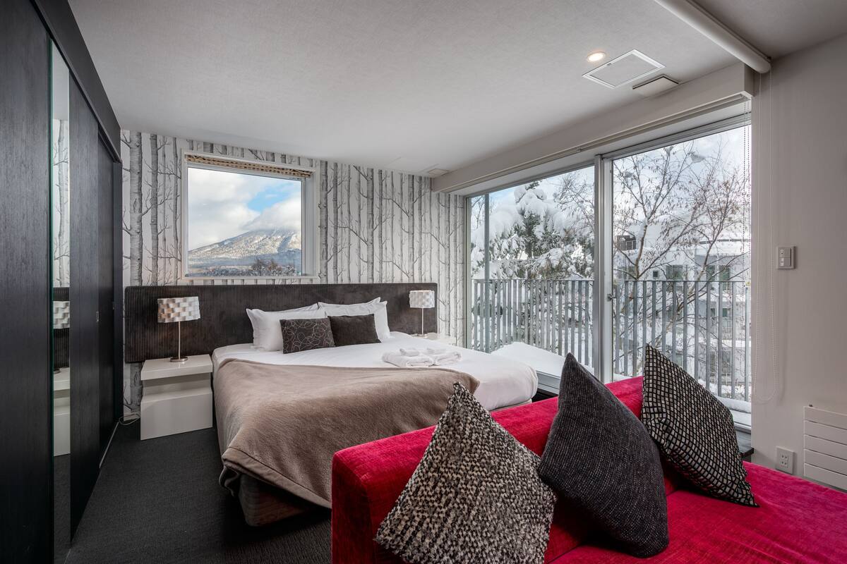 Une chambre d’hôtel moderne avec un grand lit, un canapé rouge et une vue sur une montagne enneigée.