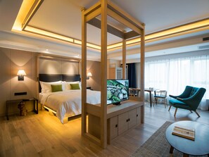 A modern hotel room with a large bed, a TV, a desk, a chair, and a window with curtains.