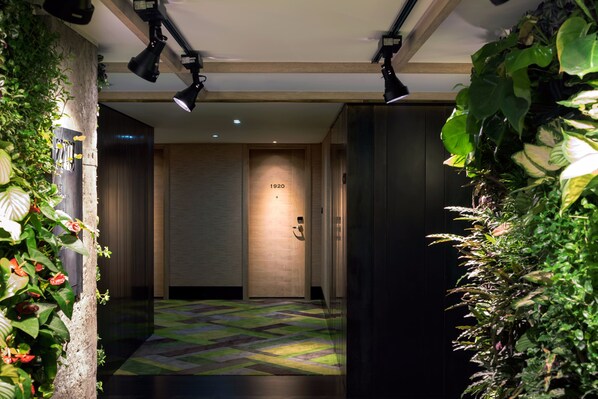 A hallway with a patterned carpet, a wooden door labeled "1920", and plants on either side.