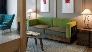 A modern hotel room with a green sofa, teal armchair, and a small coffee table. There are two wall-mounted lamps and framed artwork on the wall. - Harbin 22C Boutique Hotel (Harbin)