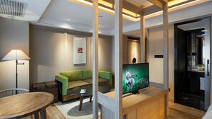 A modern hotel room with a wooden ceiling, a green sofa, a small round table, a TV on a wooden stand, and a bathroom visible through an open door. - Harbin 22C Boutique Hotel (Harbin)