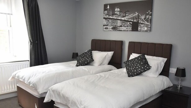 A double bed room with two nightstands, a window with curtains, and a cityscape painting on the wall. - The Red Lion (Cardigan)
