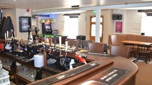 A bar area with a Guinness sign, a television, and a seating area with a table and chairs. - The Red Lion (Cardigan)