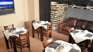 A dining area with tables set for two, each with a white tablecloth, silverware, and a teapot. There are wooden chairs and a brown leather couch in the background. - The Red Lion (Cardigan)