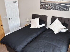 A double bed with black bedding and white pillows, a white door, and a cityscape painting on the wall. - The Red Lion (Cardigan)