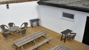 A wooden deck with picnic tables and chairs, a small table, and a window. - The Red Lion (Cardigan)