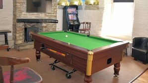 A pool table in a room with a stone wall, a fireplace, a television, and a gaming console. - The Red Lion (Cardigan)