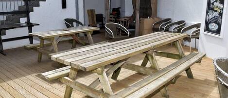 Una terraza de madera con mesas y sillas de picnic, una escalera y una pared con un cartel.