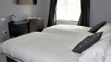 A hotel room with two beds, a desk, a chair, a flat-screen TV, and a window with curtains.