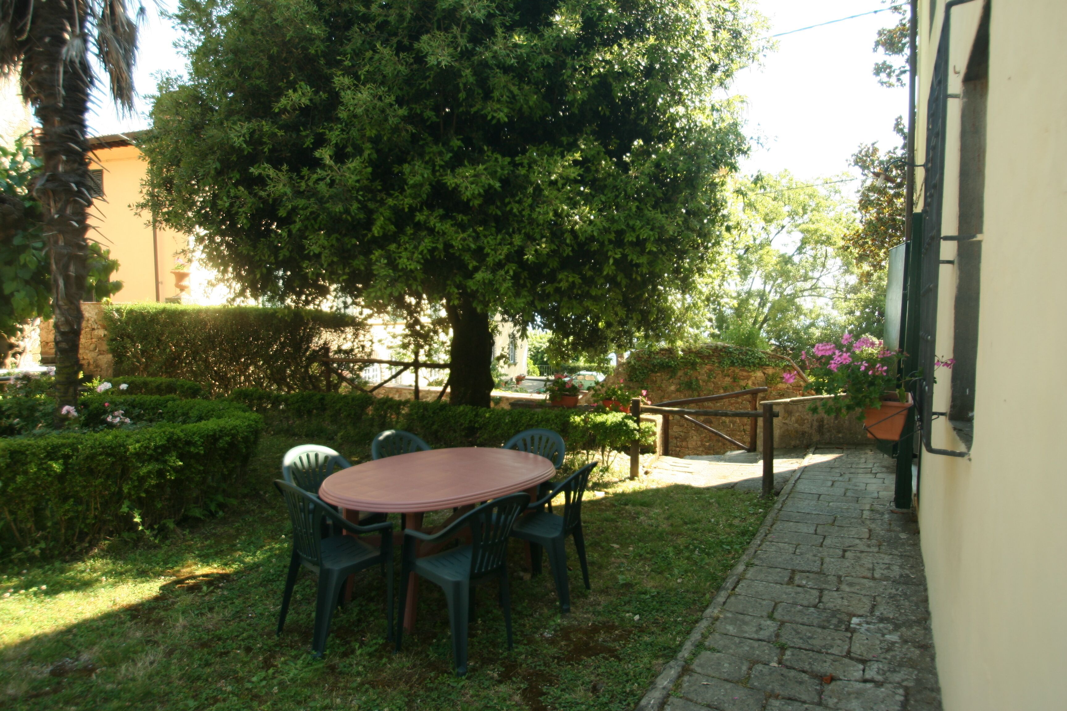 An outdoor seating area with a table and chairs, surrounded by greenery and a tree.