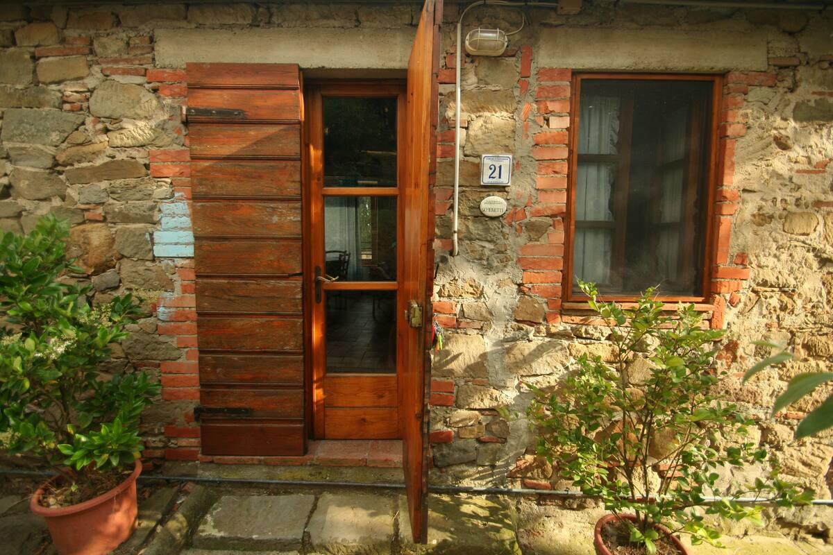 A rustic stone building with a wooden door and window, potted plants, and a number sign.