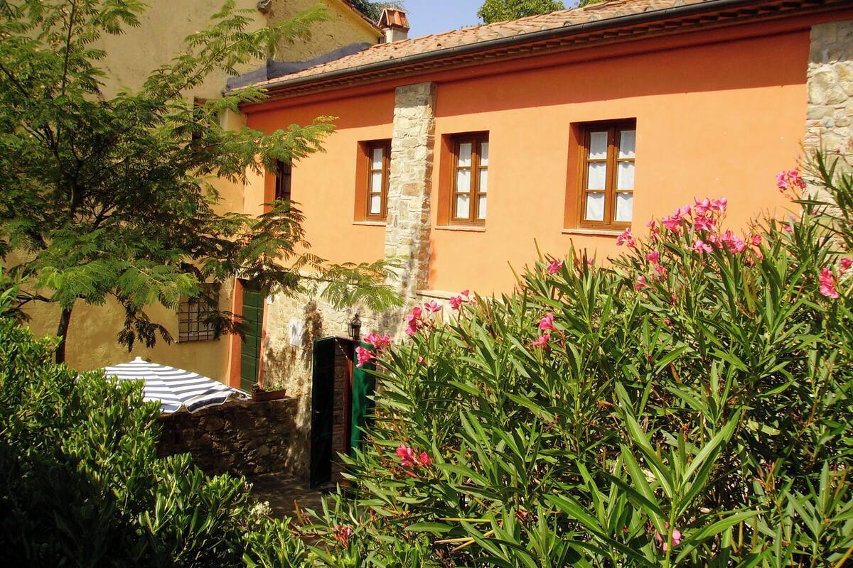 A building with a stone foundation and orange walls, featuring a small porch with a striped umbrella.