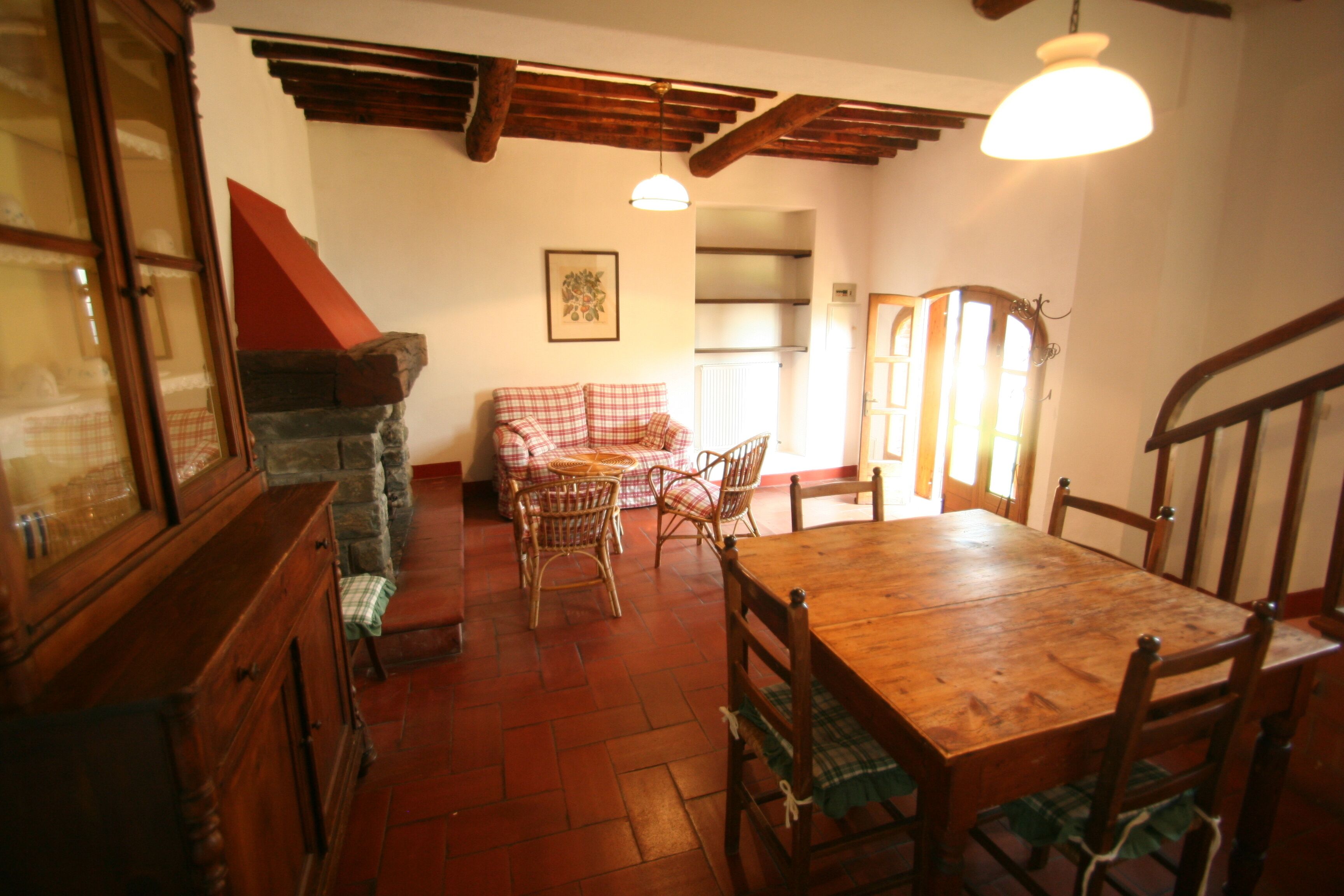 Un comedor con una mesa y sillas de madera, un sofá a cuadros, sillas de mimbre y una chimenea de piedra.