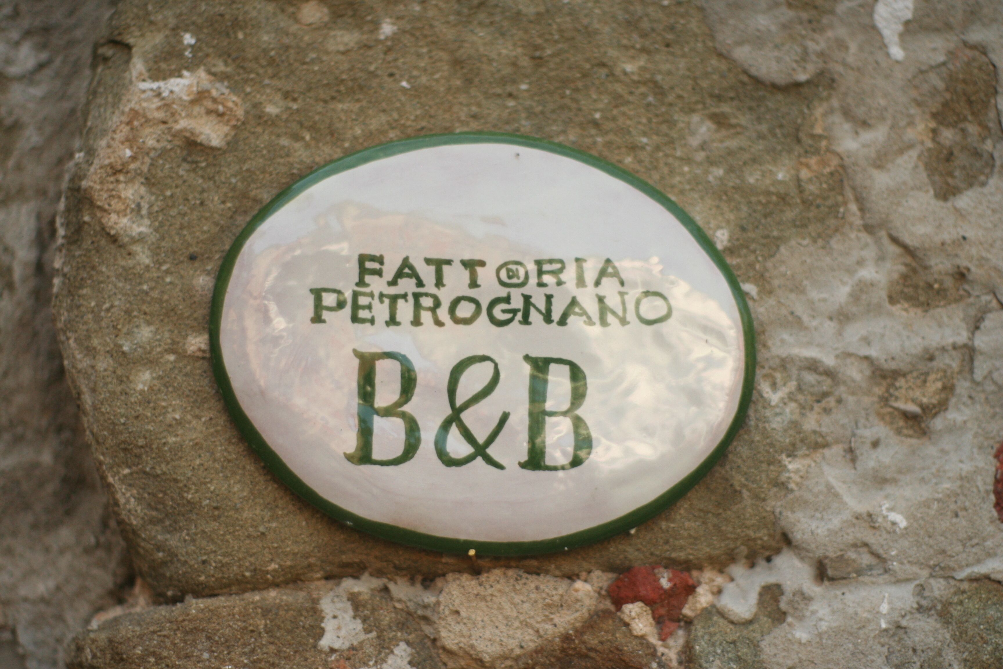 Una placa circular con la inscripción "Fattoria Petrogna B&B" en una pared de piedra.