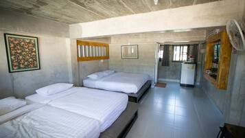 A hotel room with three beds, a fan, a refrigerator, and a door leading to another room.