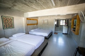 A hotel room with three beds, a fan, a refrigerator, and a door leading to another room.