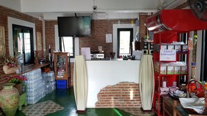Una cocina con pared de ladrillo, televisor de pantalla plana, mostrador con diversos objetos y un ventilador rojo.