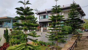 Un edificio moderno con varios pisos, rodeado de abundante vegetación y una escalera que conduce a la entrada.