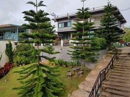 A modern building with multiple floors, surrounded by lush greenery and a staircase leading up to the entrance.