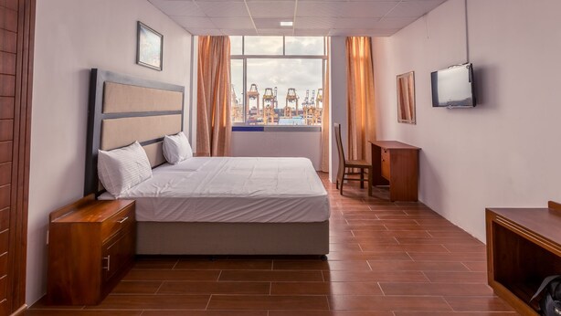 A hotel room with a large bed, wooden nightstands, a desk, a chair, a TV, and a window with a view of cranes. - Metro Port City Hotel (Colombo)
