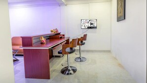 A reception area with a wooden desk, two bar stools, a sofa, and a flat-screen TV mounted on the wall. - Metro Port City Hotel (Colombo)