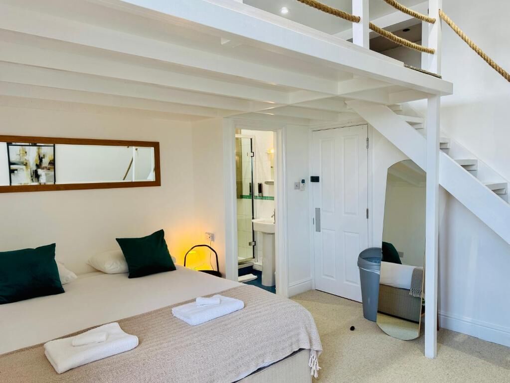 A bedroom with a bed, a mirror, a staircase, and a bathroom visible through an open door.