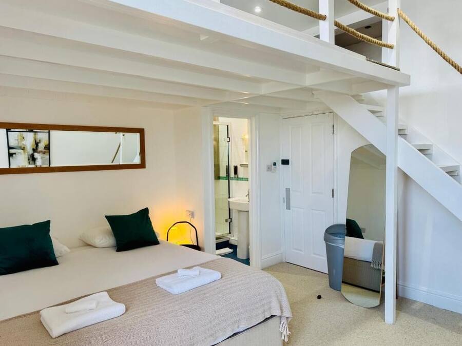 A bedroom with a bed, a mirror, a staircase, and a bathroom visible through an open door.