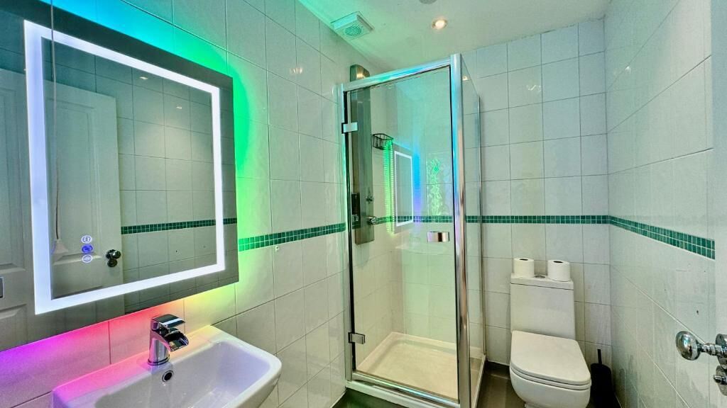 Un baño con ducha envuelta en vidrio, un lavamanos, un inodoro y un espejo con iluminación LED.