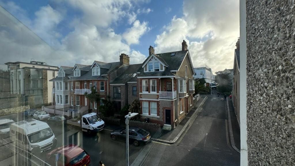 Una calle residencial con casas, autos estacionados y cielo despejado.