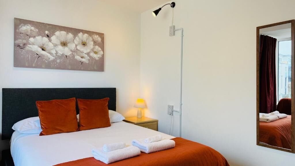 A hotel room with a bed, a nightstand, a lamp, a painting, and a mirror.