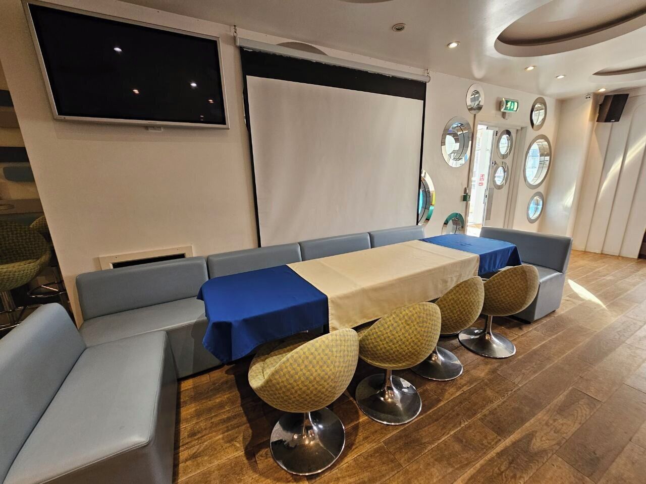 Comedor con una mesa larga, asientos tapizados en azul y beige, y piso de madera.