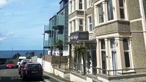 A coastal hotel with a modern facade, a prominent sign for Reel Lodge, and a view of the sea. - Reef Lodge (Newquay)