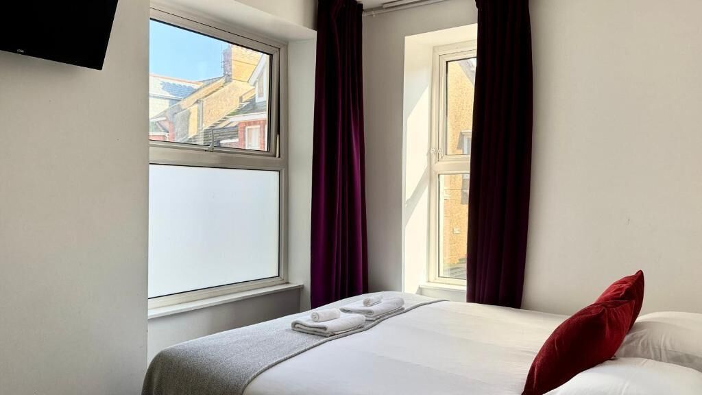 Quarto de hotel com cama, janela e televisão na parede.