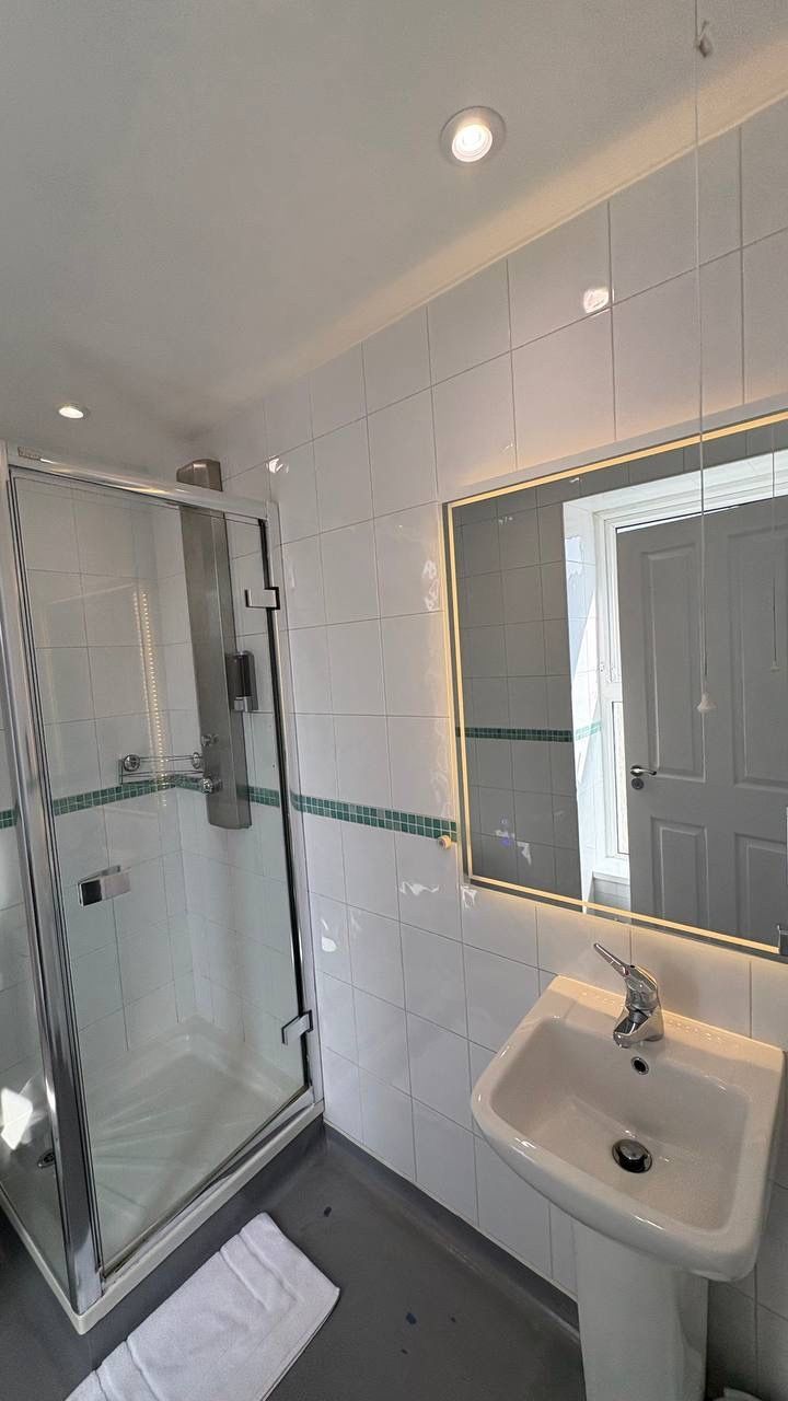 A bathroom with a glass shower enclosure, a white sink, and a mirror with a light strip.