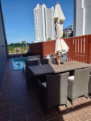Een balkon met een zwembad, rieten meubilair en uitzicht op hoge gebouwen.