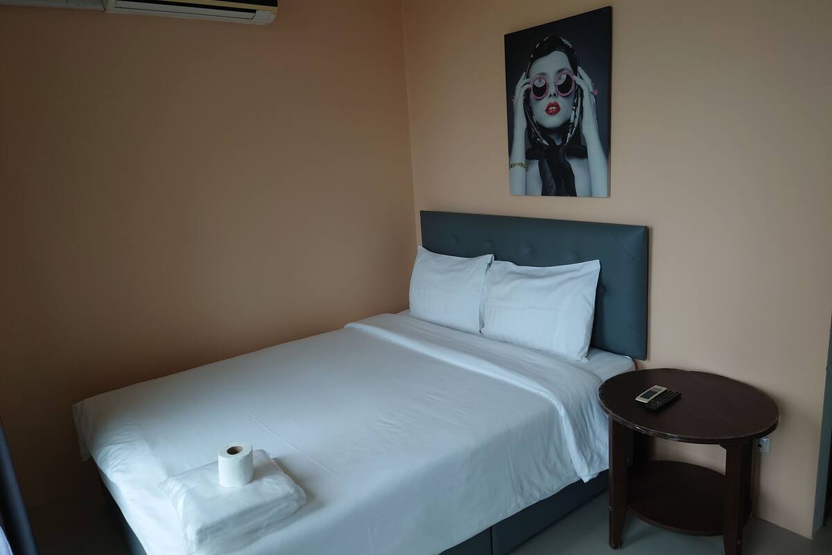 A hotel room with a bed, a round wooden table, a wall-mounted air conditioner, and a painting.