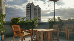 A rooftop terrace with wooden furniture and a view of tall buildings. - Baan der Bruyn (Pattaya)