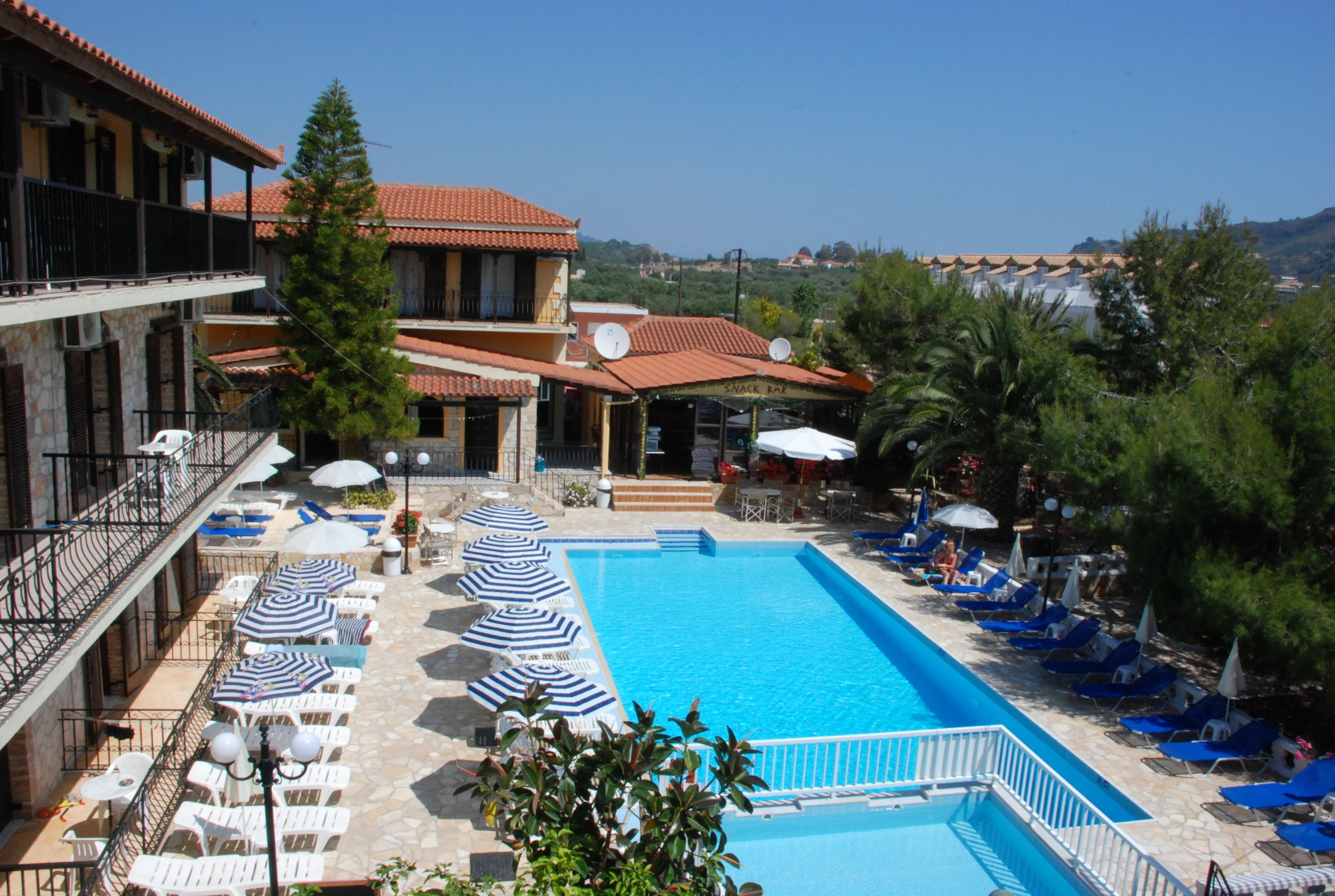 Un espace piscine avec des chaises longues et des parasols, un bâtiment doté de balcons et une vue dégagée sur le paysage environnant.