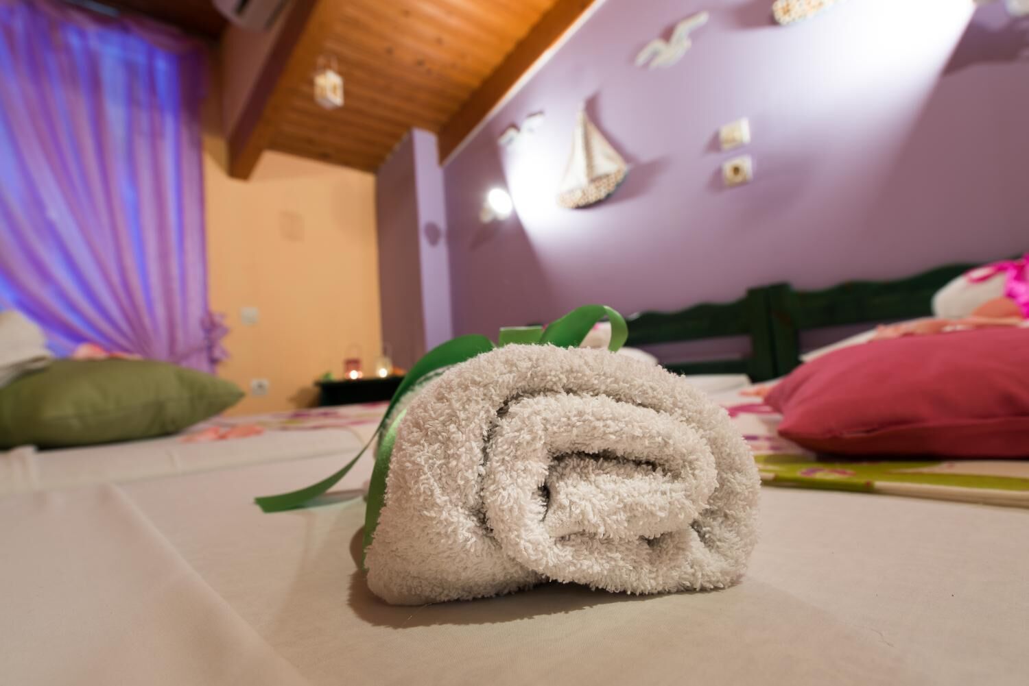 A neatly made bed with a rolled towel in the center, a green pillow to the left, and a pink pillow to the right.