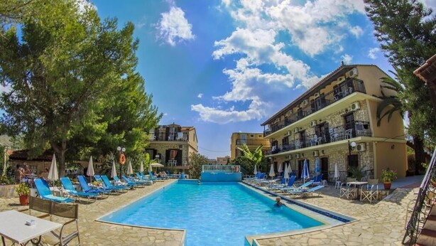 A swimming pool with lounge chairs and umbrellas, surrounded by stone buildings with balconies. - Elena Studios (Zakynthos)