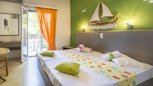 A hotel room with two beds, a balcony with orange curtains, a sailboat decoration on the wall, and a small table with a chair. - Elena Studios (Zakynthos)
