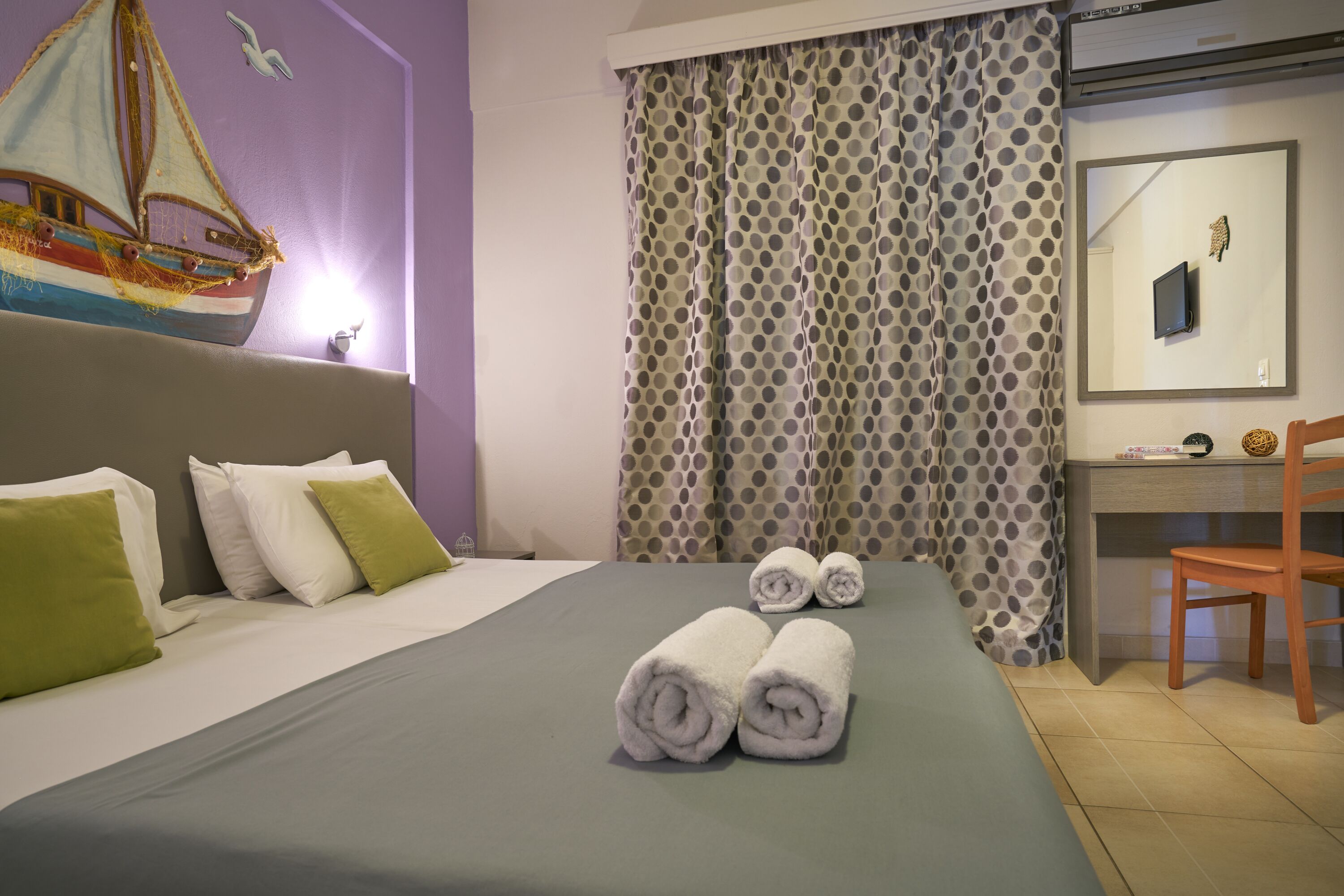 Una cama bien hecha con almohadas, un escritorio con silla y una cortina de lunares.