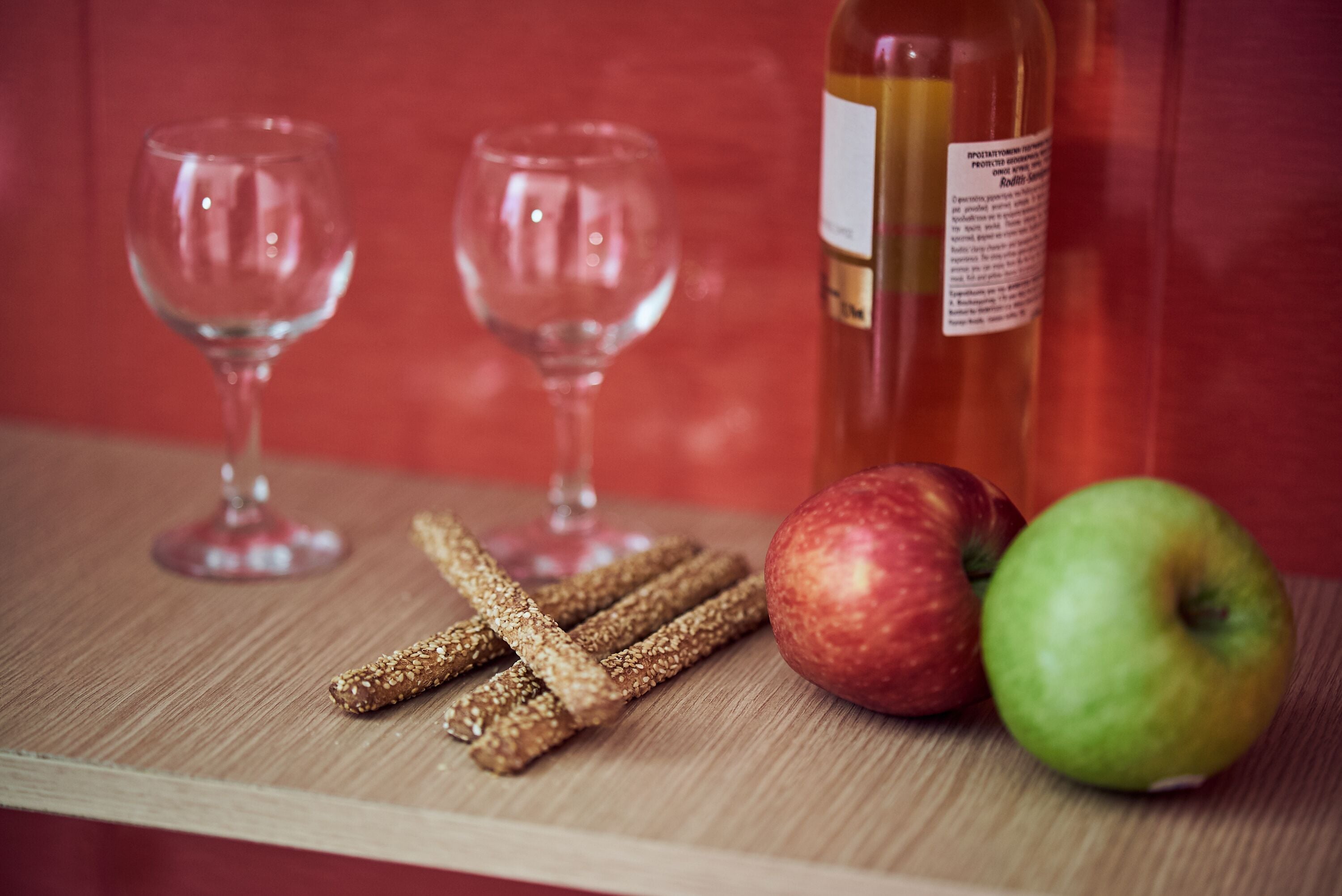 Un tavolo di legno con una bottiglia di vino, due bicchieri da vino vuoti e due mele.