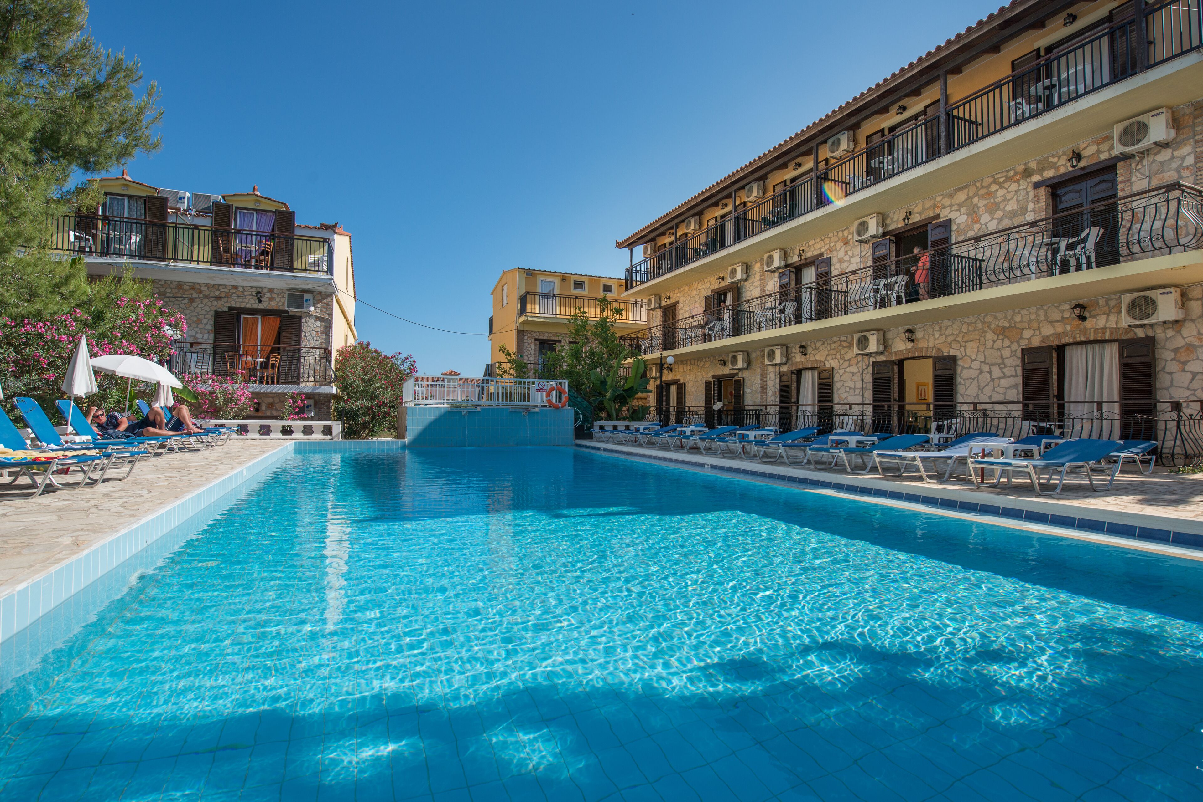 Une piscine entourée de chaises longues, elle-même bordée d’immeubles à plusieurs étages dotés de balcons et de climatiseurs.