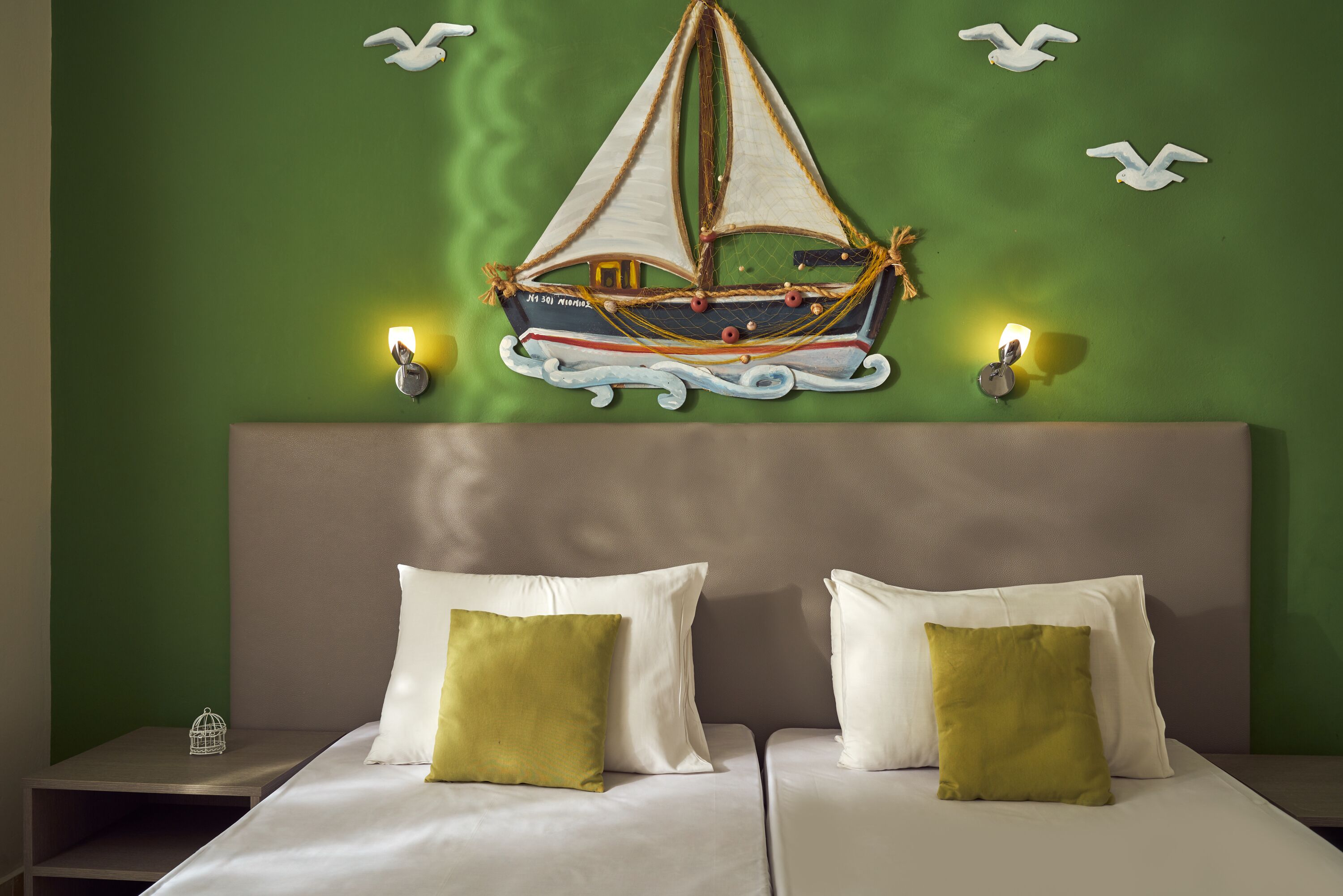 Una habitación con cama, dos almohadas, un adorno náutico en la pared y dos apliques.