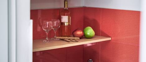 A kitchen with a wooden shelf holding a wine bottle, glasses, and apples.