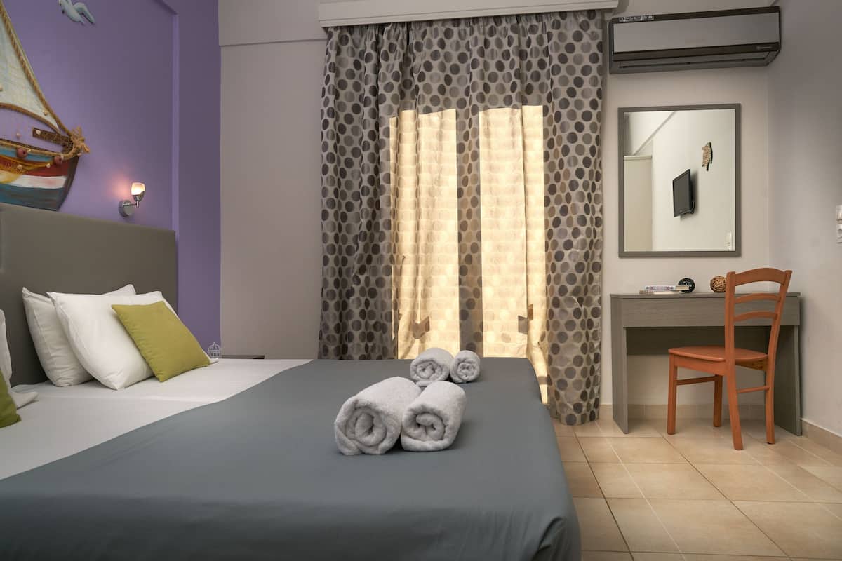 A neatly made bed with rolled towels, a desk with a chair, and a mirror.